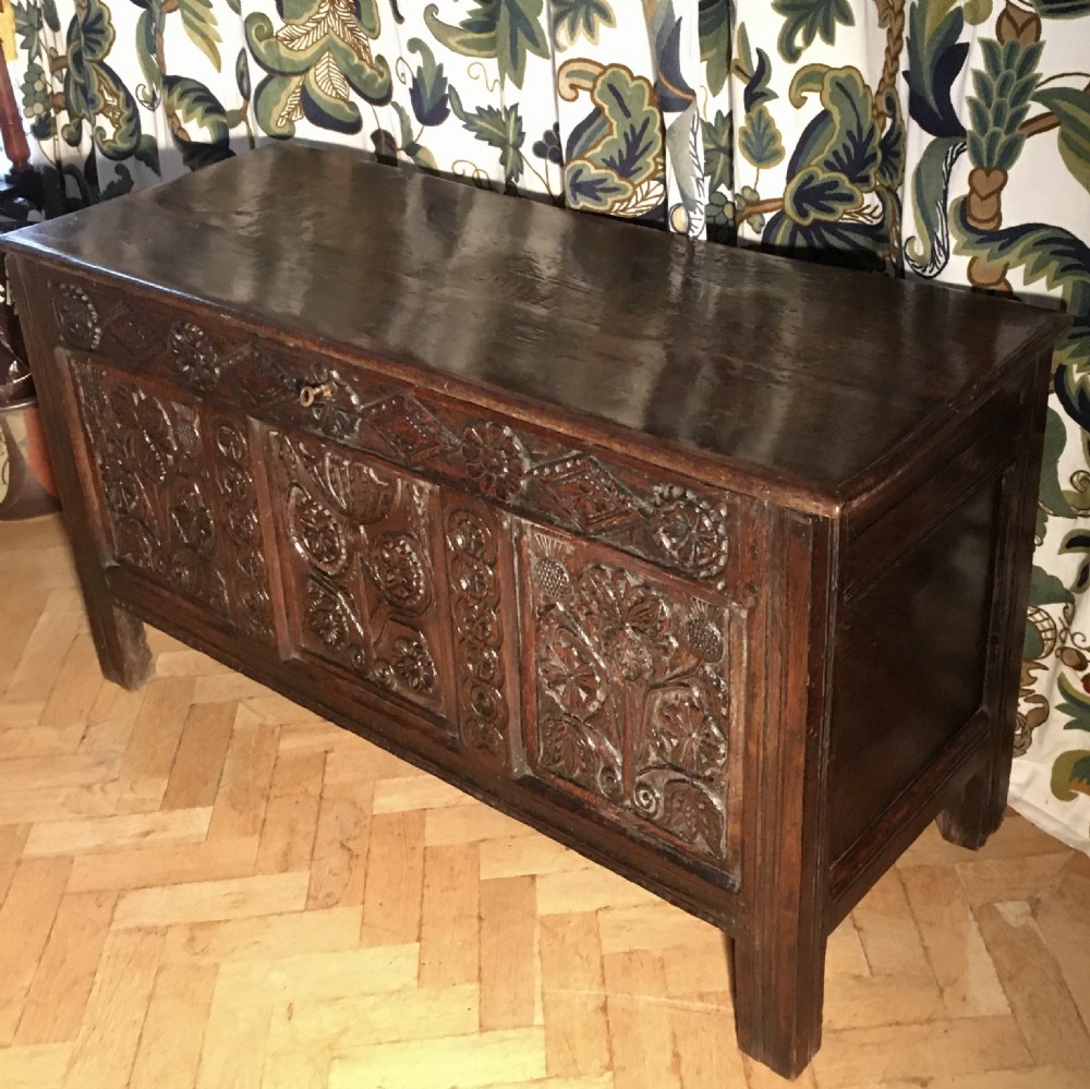 A dark carved oak coffer featuring three detailed floral front panels, a carved top rail, and a flat hinged rectangular lid. View II