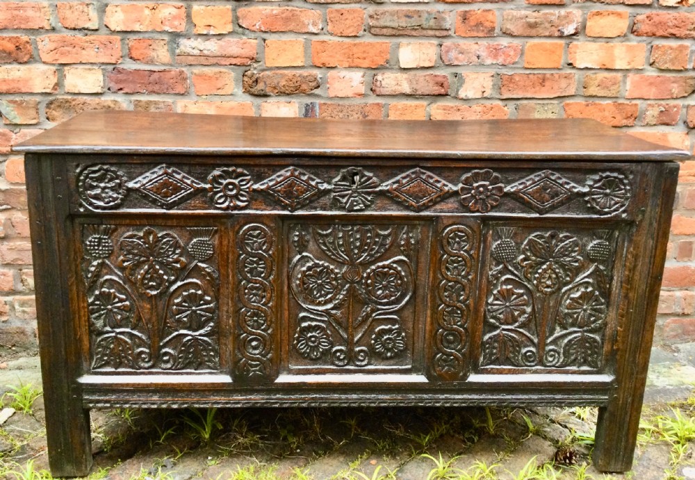 A dark carved oak coffer featuring three detailed floral front panels, a carved top rail, and a flat hinged rectangular lid. View VII