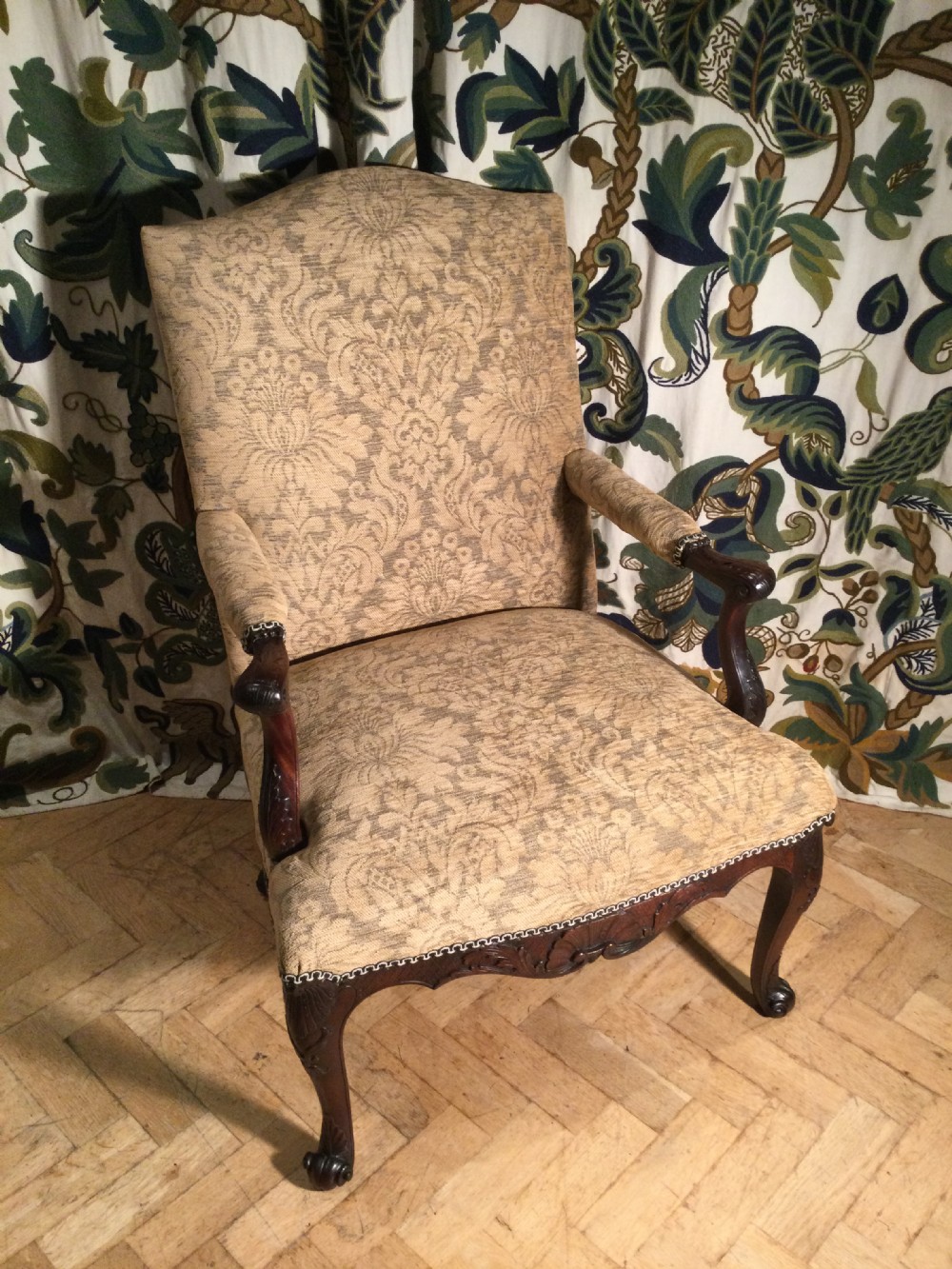 An upholstered open armchair featuring dark mahogany carved cabriole legs and patterned beige fabric upholstery.
