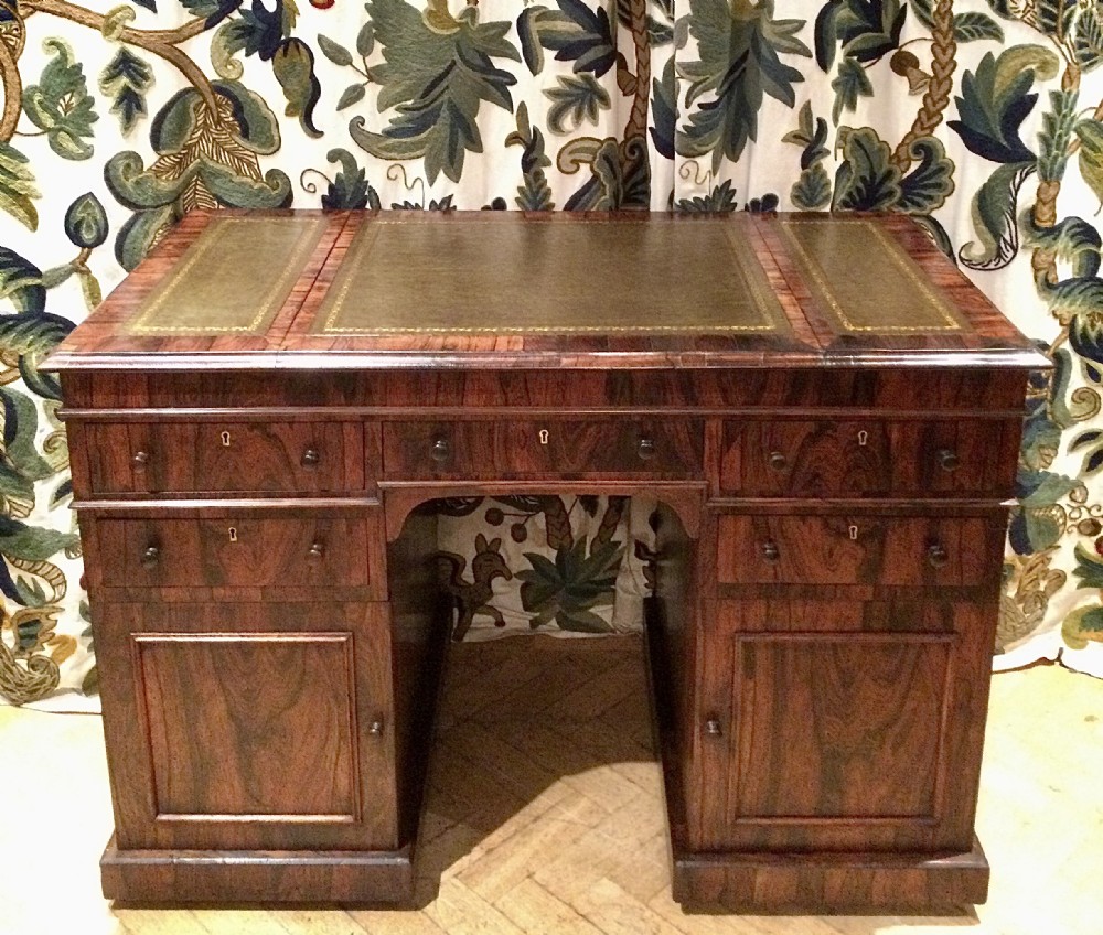 An antique dark rosewood pedestal desk featuring three green leather writing inserts with gold tooling, upper drawers, and lower panelled pedestal cupboards.