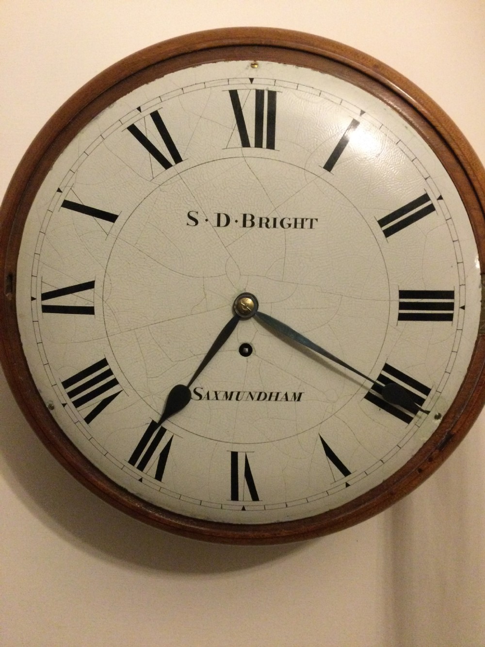 A circular Victorian dial wall clock featuring a warm mahogany bezel, an off-white painted dial with craquelure, black Roman numerals, and steel spade hands.