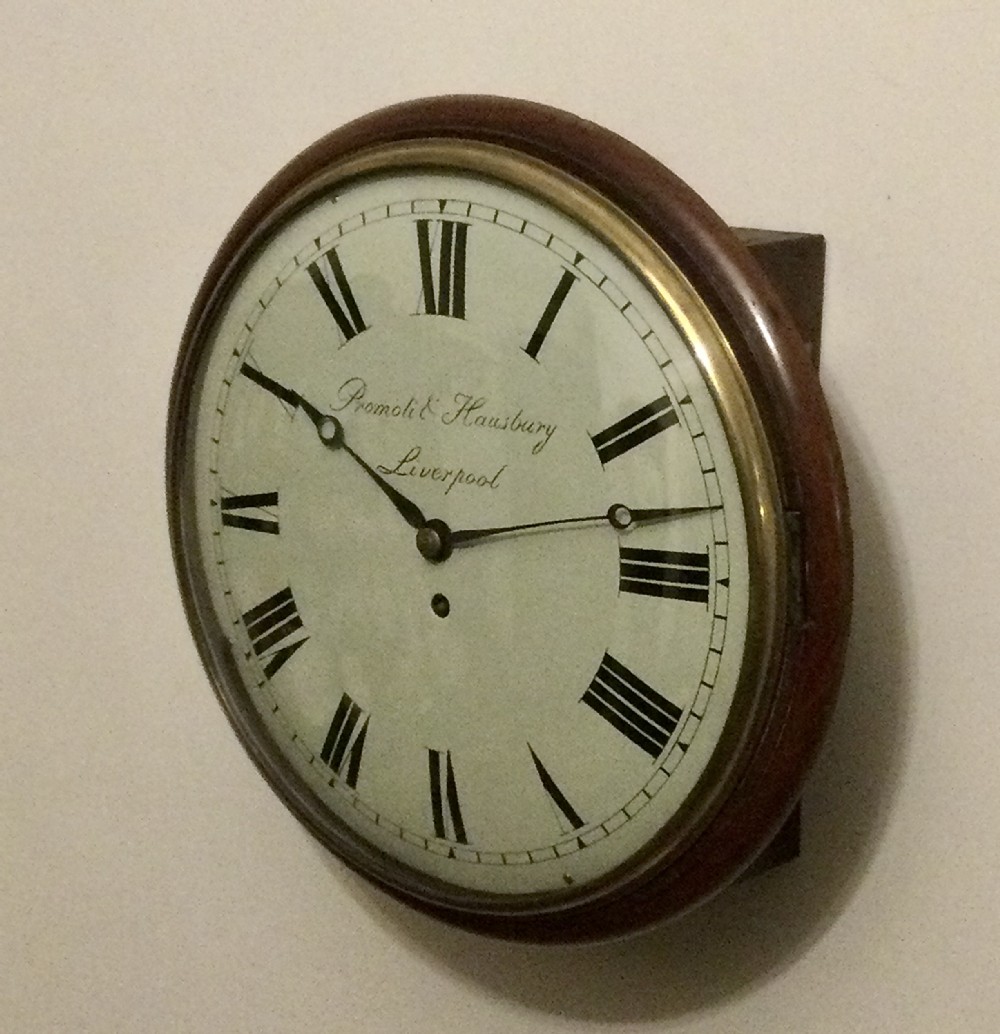 A circular Victorian wall clock featuring a mahogany wood surround, brass bezel, and white face with black Roman numerals.