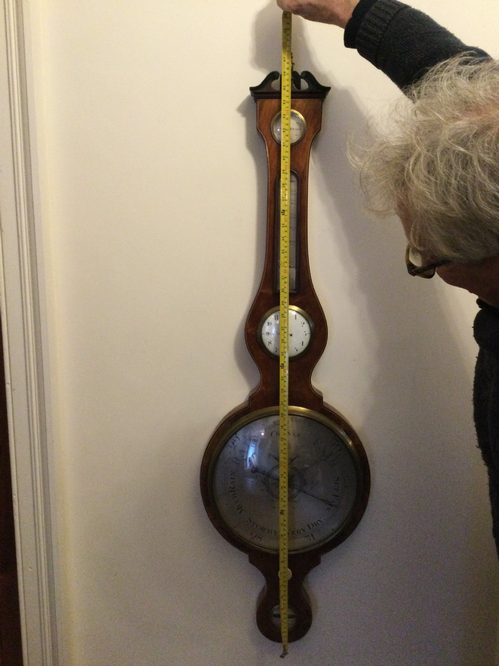 A wall-mounted Georgian mahogany banjo barometer featuring a swan-neck pediment, brass finial, hygrometer dial, central spirit thermometer, and lower dial. View II