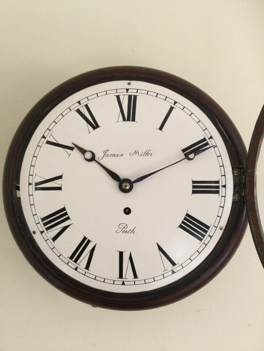 A circular antique wall clock featuring a dark mahogany case, a brass bezel, and a cream dial with black Roman numerals signed James Miller Perth. View III