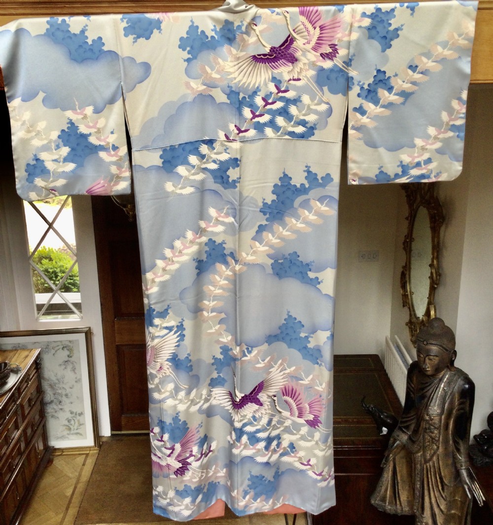 A full-length Japanese silk kimono in light blue decorated with flying purple and white cranes among stylized cloud motifs.