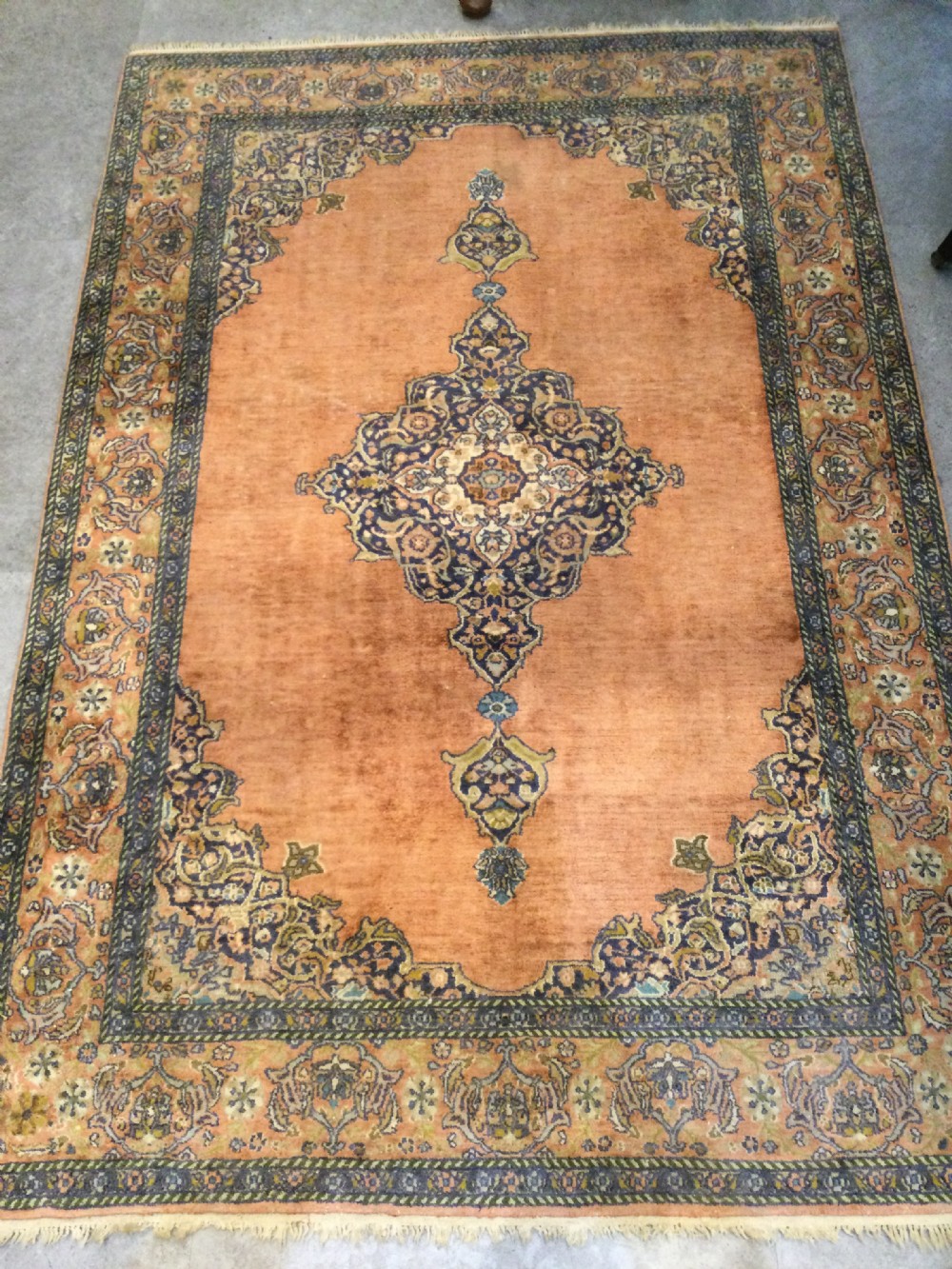 A rectangular hand-knotted wool rug featuring a central navy and cream medallion on a terracotta field with patterned spandrels and a multi-banded border. View III