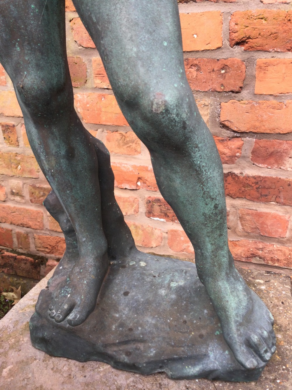 A cast bronze statue depicting a classical male nude figure in a contrapposto pose with a weathered verdigris patina. View VI