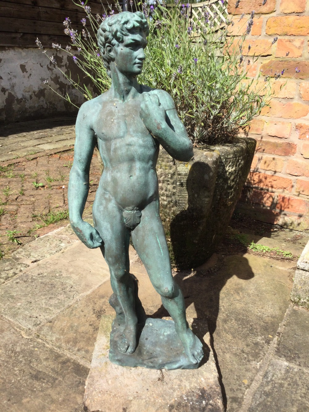 A cast bronze statue depicting a classical male nude figure in a contrapposto pose with a weathered verdigris patina. View IX