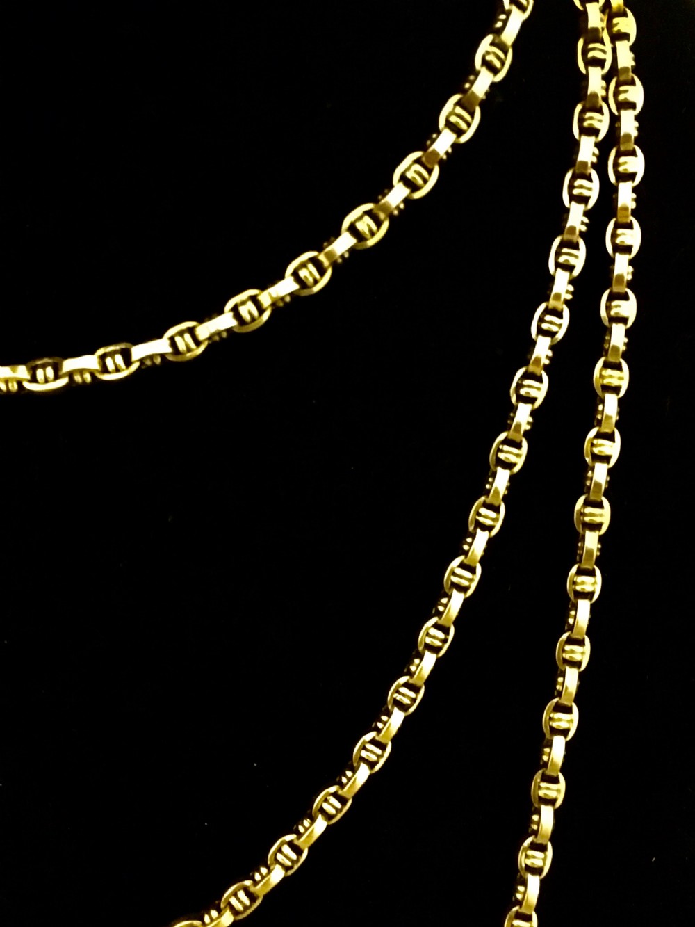 A long yellow gold link chain displayed in multiple loops against a dark background. View V