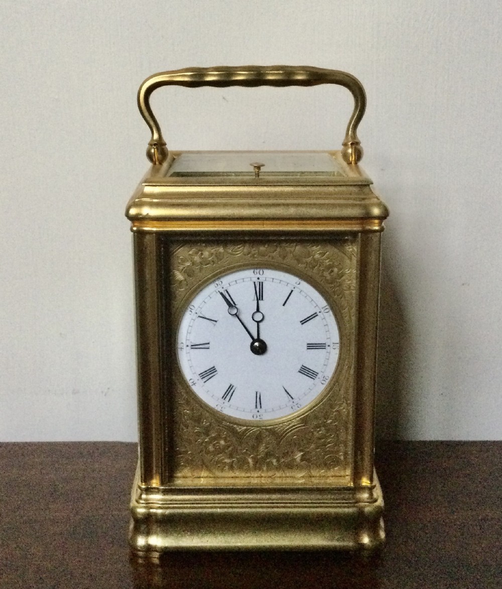 A 19th-century French gilt brass carriage clock featuring an engraved face plate, white enamel circular dial with Roman numerals, and a hinged top handle.