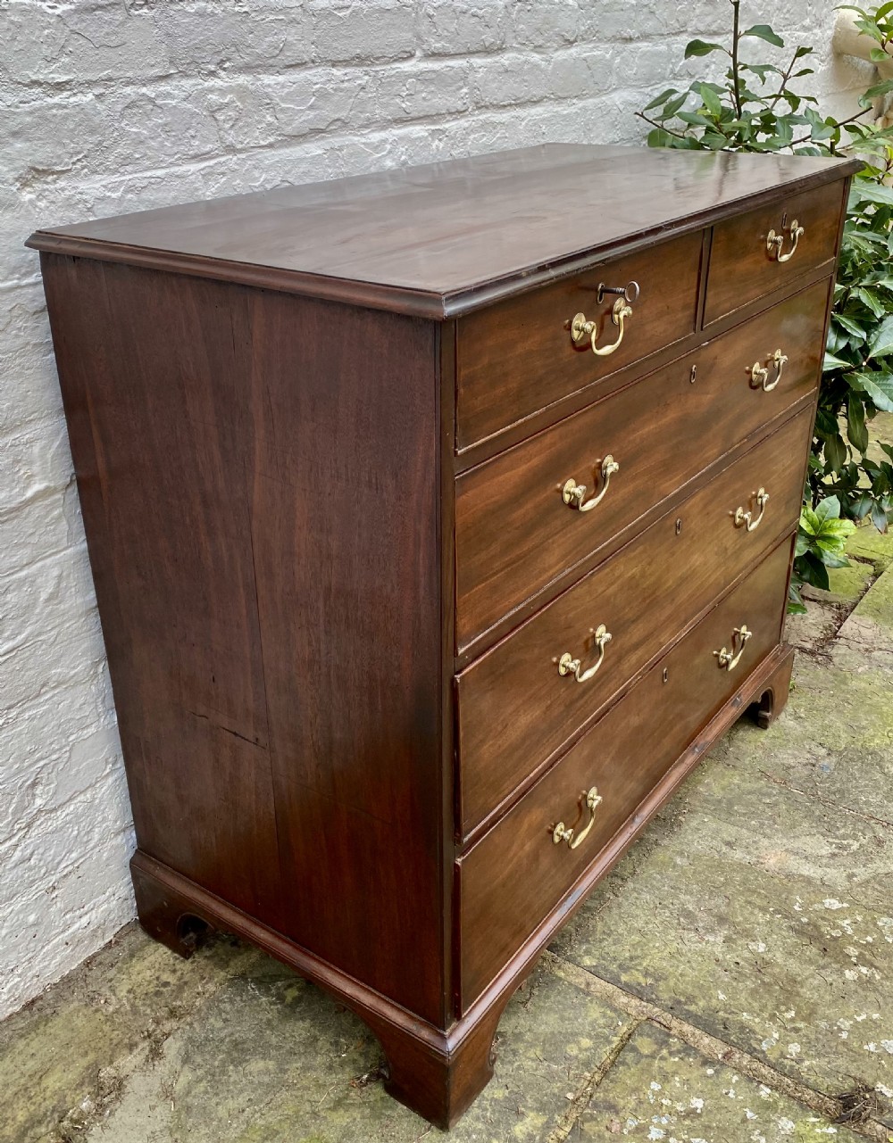 A Georgian mahogany chest of drawers featuring two short drawers over three long drawers with brass swan-neck handles and shaped bracket feet. View II