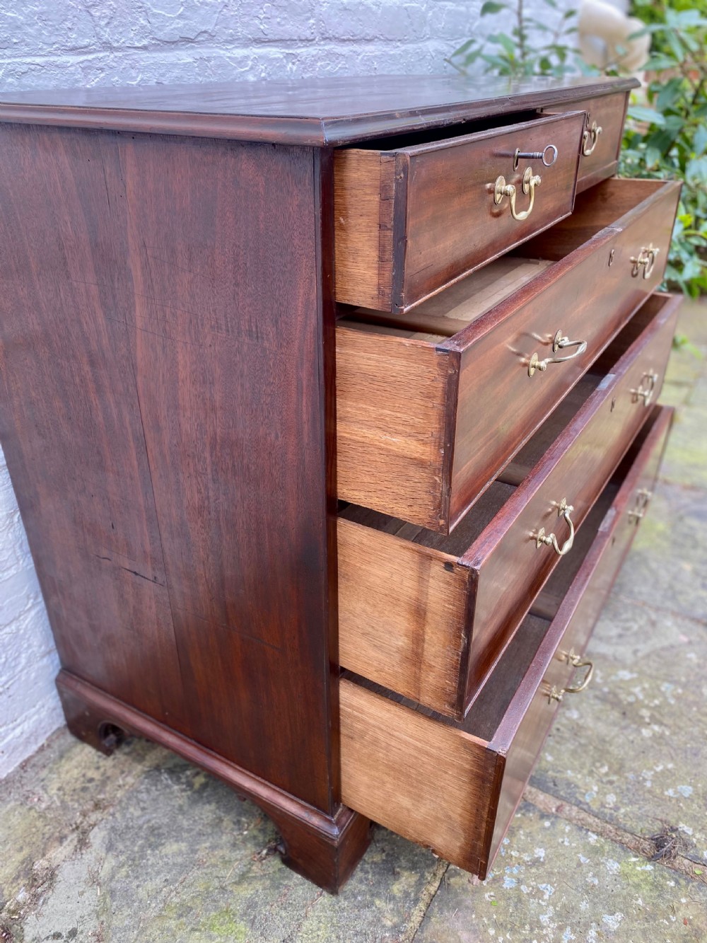 A Georgian mahogany chest of drawers featuring two short drawers over three long drawers with brass swan-neck handles and shaped bracket feet. View V