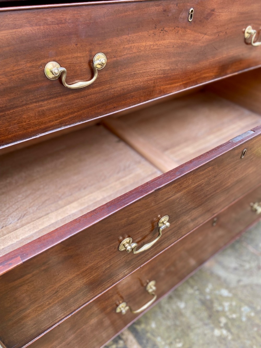A Georgian mahogany chest of drawers featuring two short drawers over three long drawers with brass swan-neck handles and shaped bracket feet. View VI