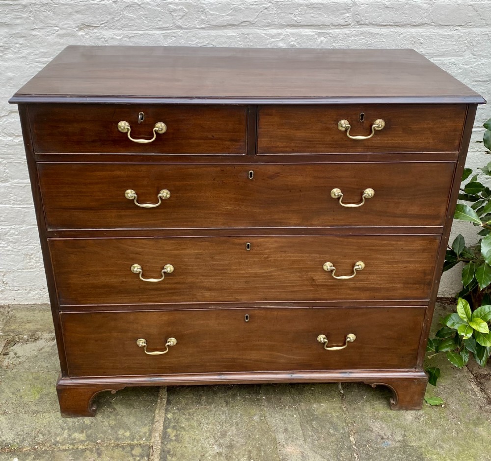 A Georgian mahogany chest of drawers featuring two short drawers over three long drawers with brass swan-neck handles and shaped bracket feet. View VII