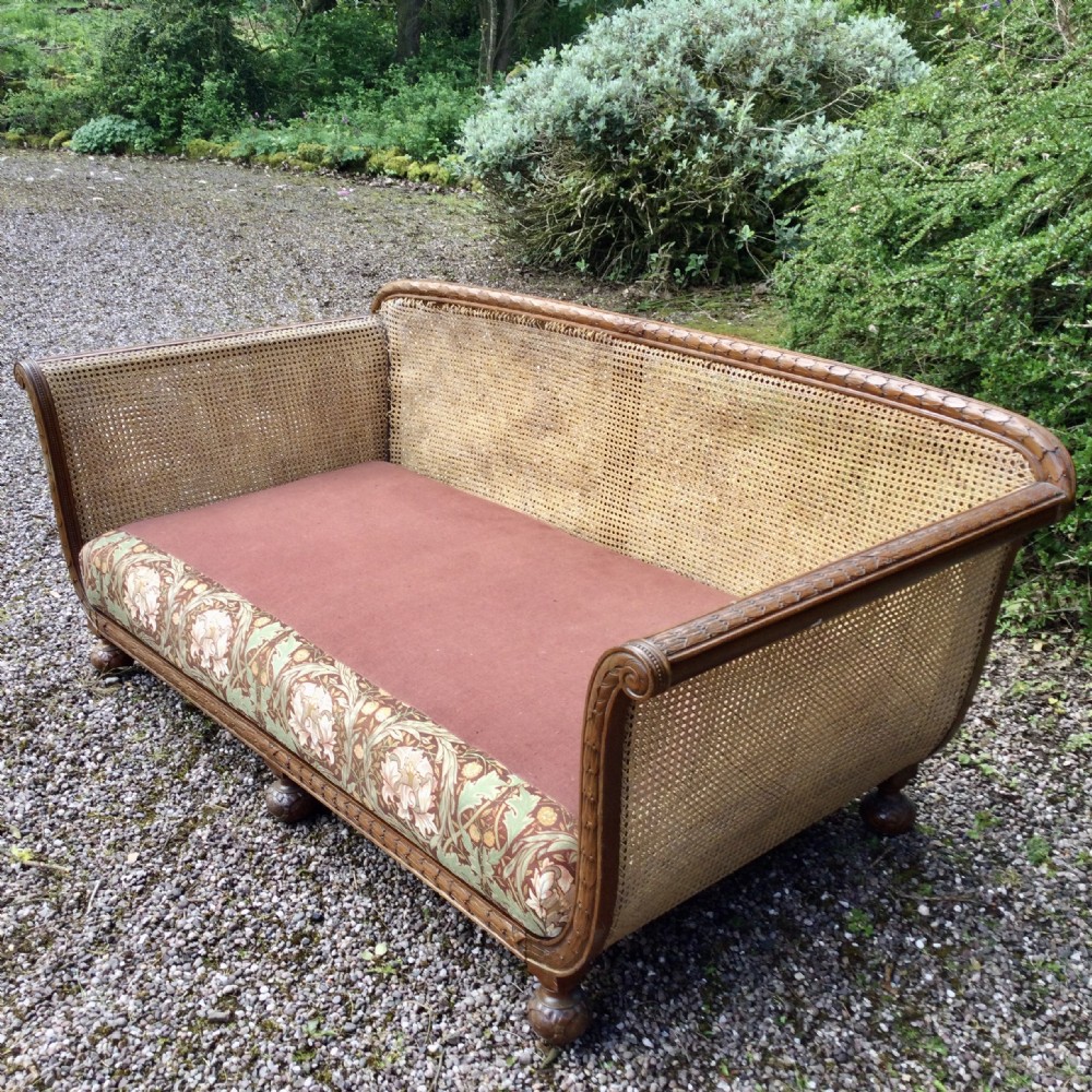 A French caned bergere sofa with a carved walnut frame, double-walled woven cane back, and a fabric seat cushion.