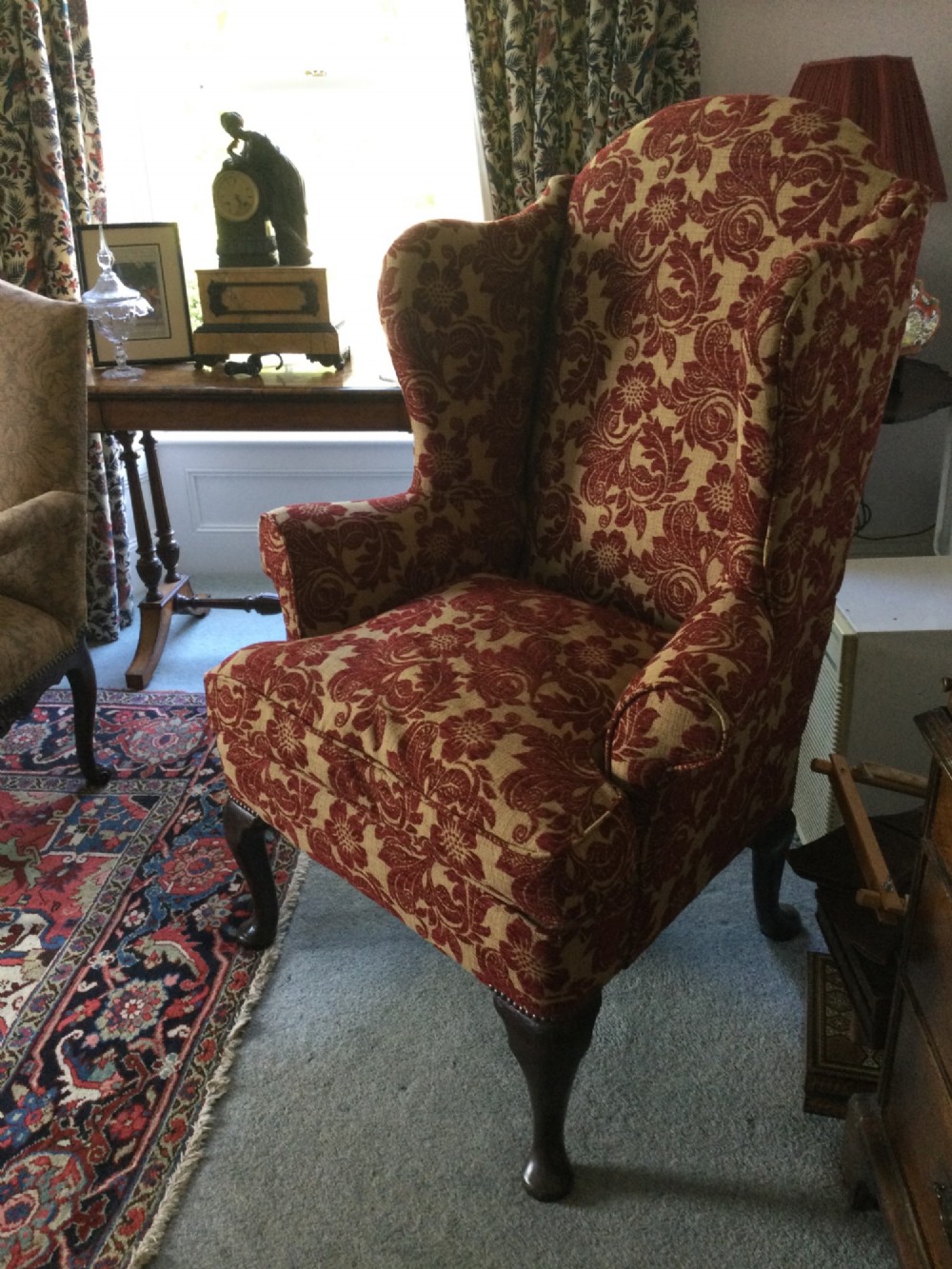 A traditional high-backed wing armchair upholstered in red and beige floral damask fabric with dark wooden cabriole legs. View II