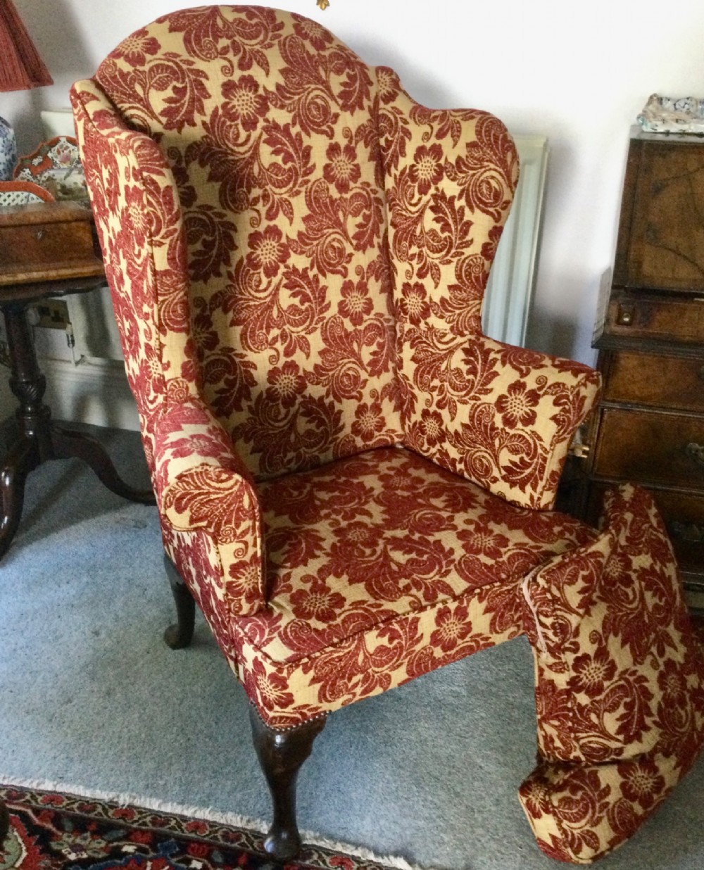 A traditional high-backed wing armchair upholstered in red and beige floral damask fabric with dark wooden cabriole legs. View III
