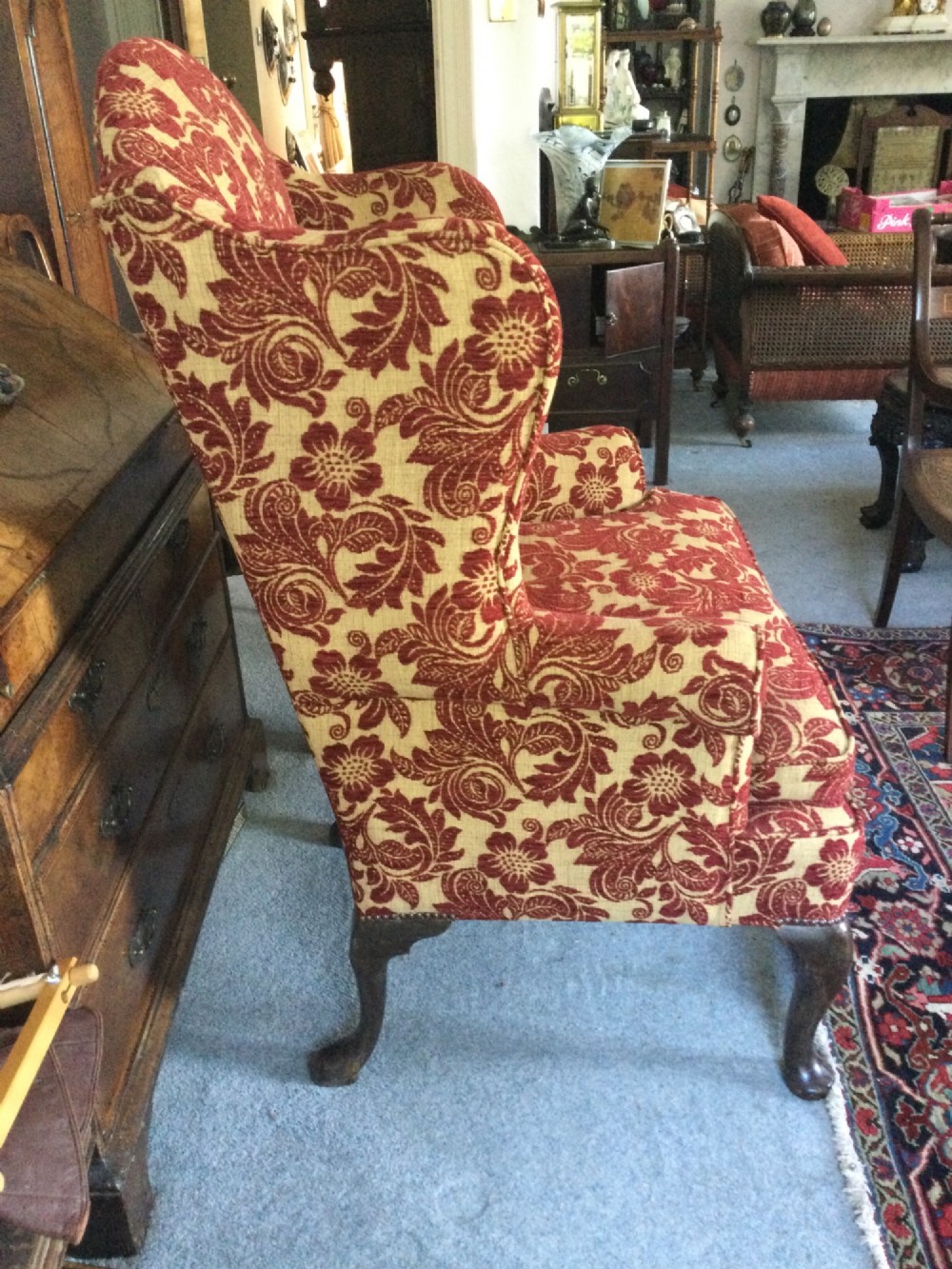 A traditional high-backed wing armchair upholstered in red and beige floral damask fabric with dark wooden cabriole legs. View IV