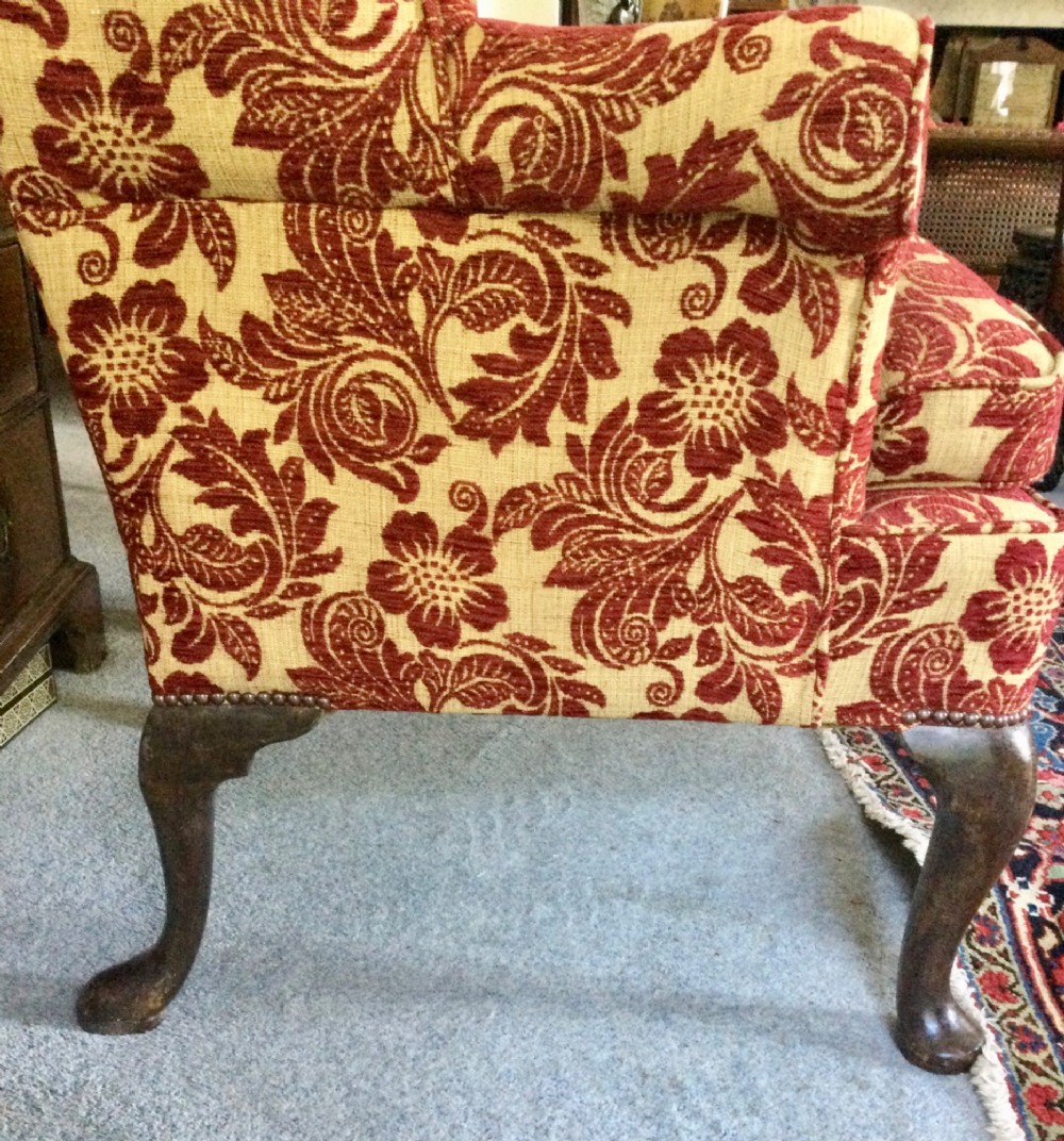 A traditional high-backed wing armchair upholstered in red and beige floral damask fabric with dark wooden cabriole legs. View V