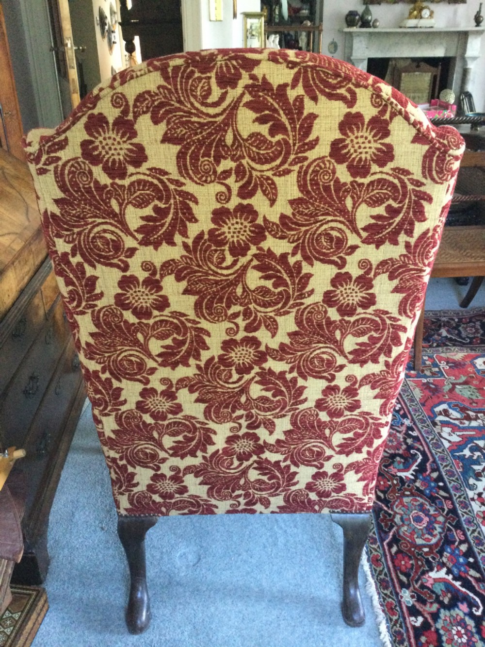 A traditional high-backed wing armchair upholstered in red and beige floral damask fabric with dark wooden cabriole legs. View VI