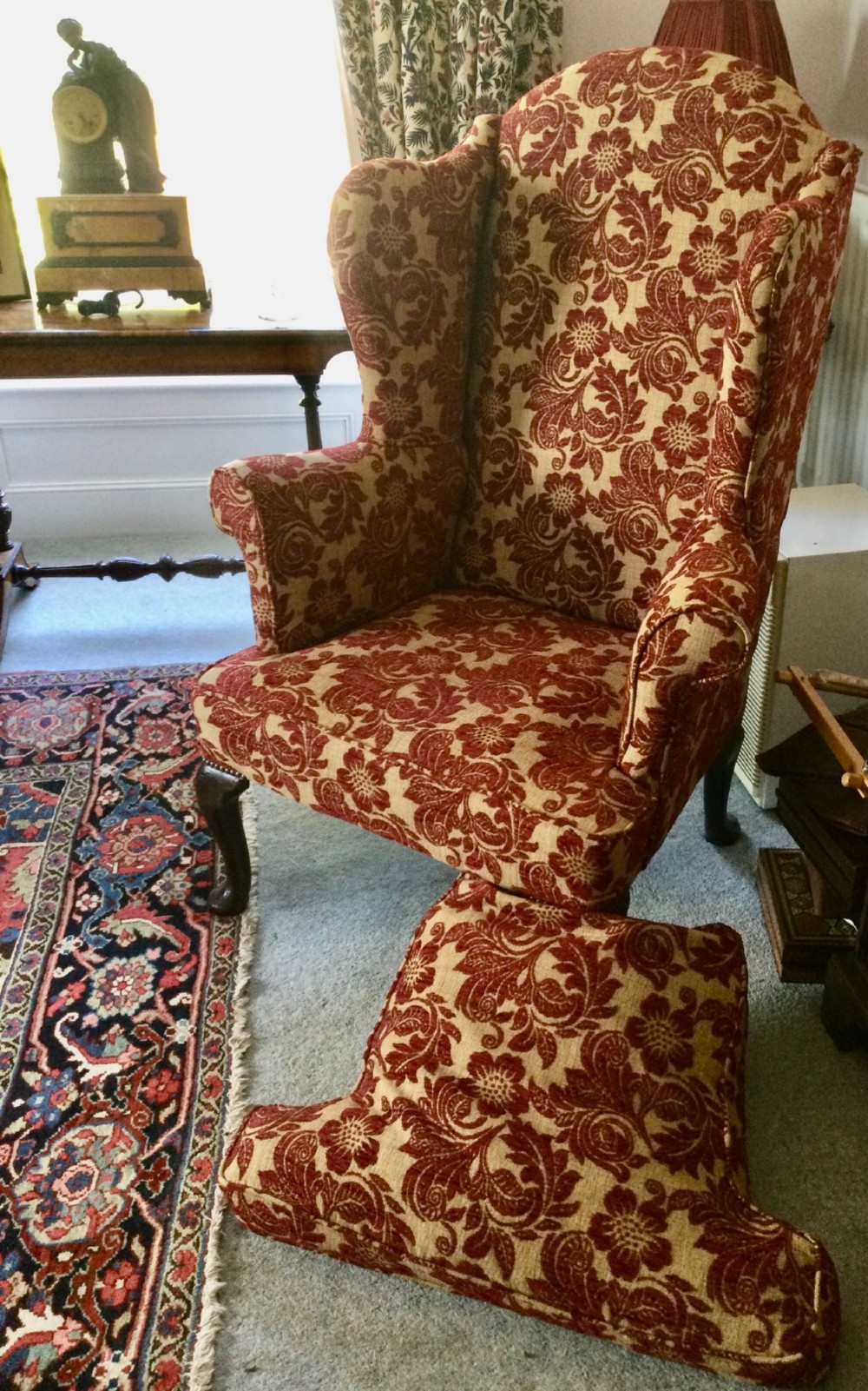 A traditional high-backed wing armchair upholstered in red and beige floral damask fabric with dark wooden cabriole legs. View VII