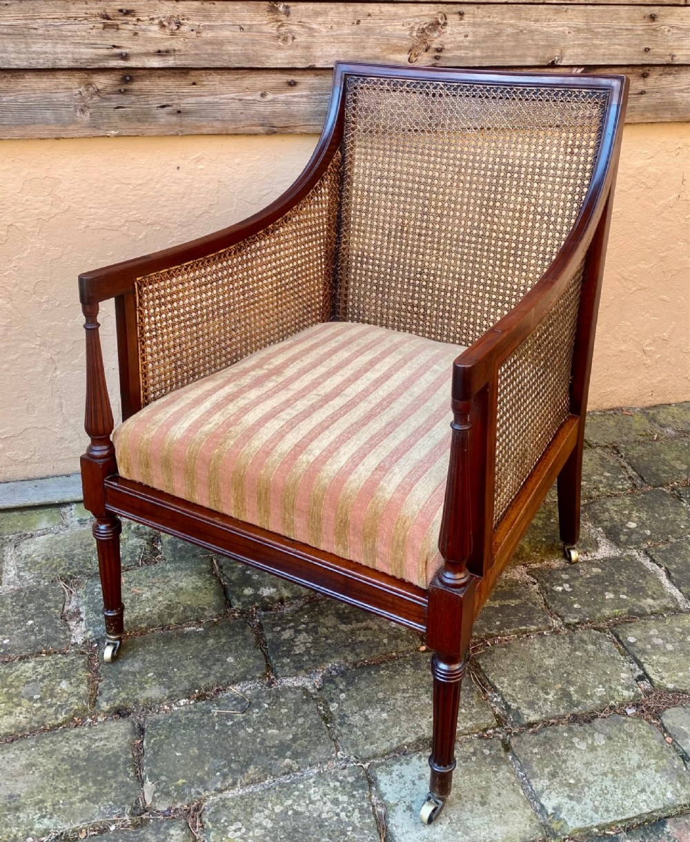An antique mahogany armchair featuring woven cane back and side panels, turned front legs with brass castors, and a striped fabric seat cushion. View II