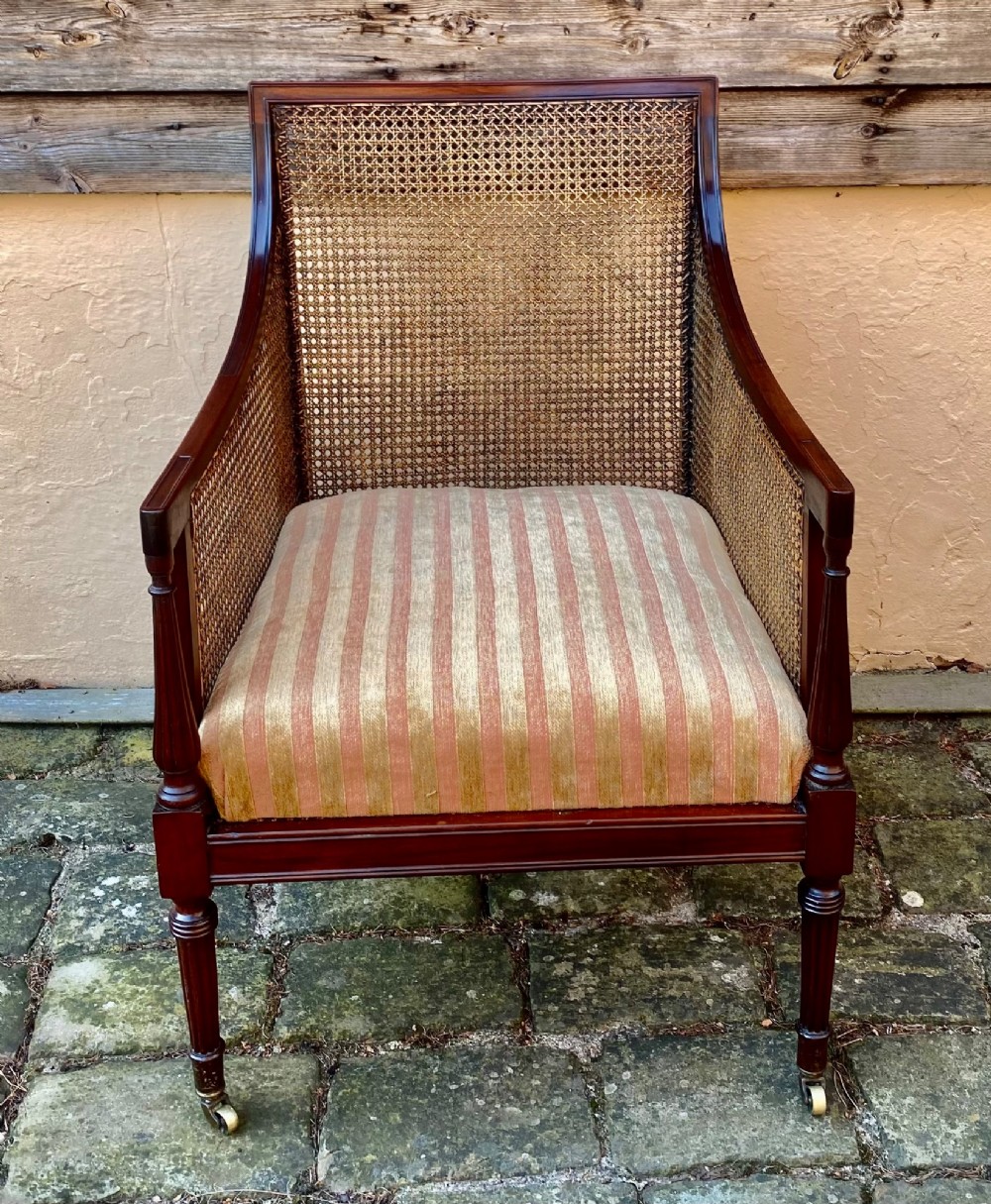 An antique mahogany armchair featuring woven cane back and side panels, turned front legs with brass castors, and a striped fabric seat cushion. View III