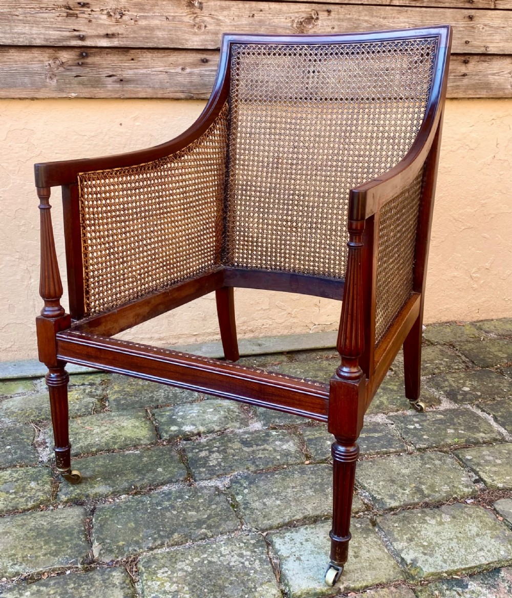 An antique mahogany armchair featuring woven cane back and side panels, turned front legs with brass castors, and a striped fabric seat cushion. View VI
