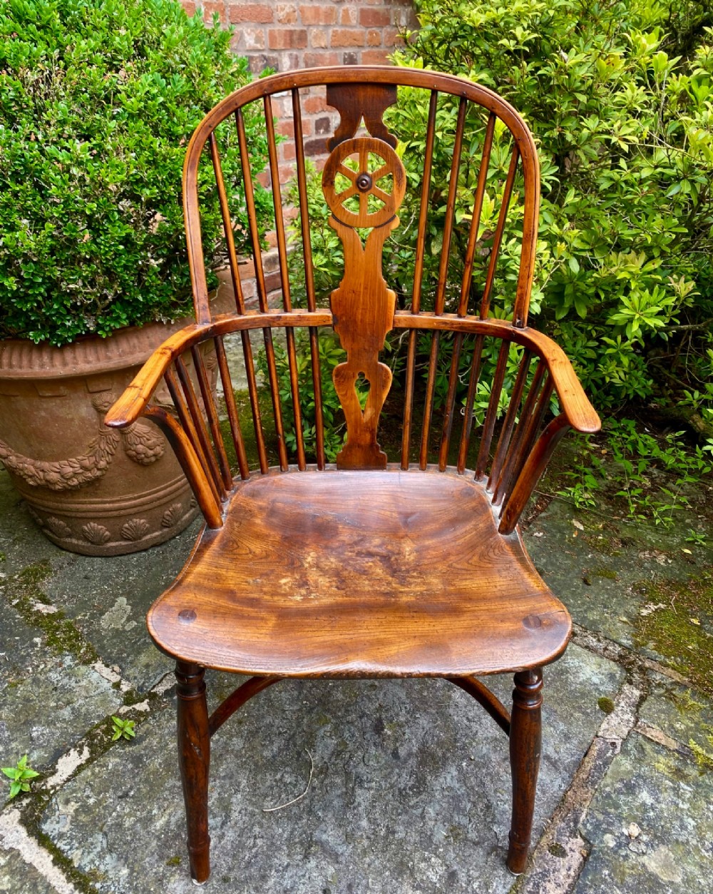 An antique yew wood Windsor armchair featuring a hoop back with a decorative wheelback splat, shaped saddle seat, and turned legs.
