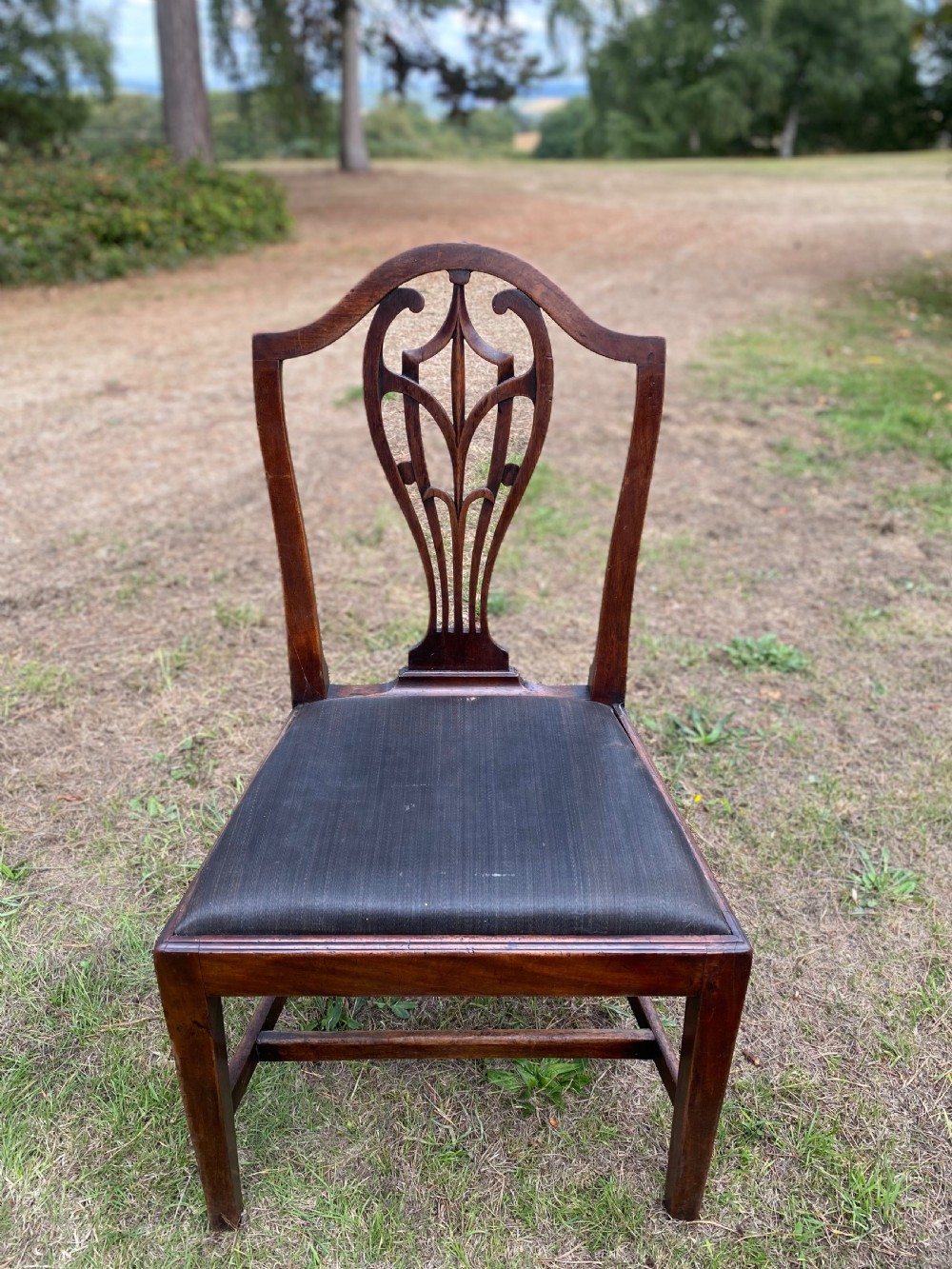 A set of mahogany dining chairs featuring carved openwork back splats, shaped armrests on the carver chairs, and dark fabric upholstered seat pads. View VIII