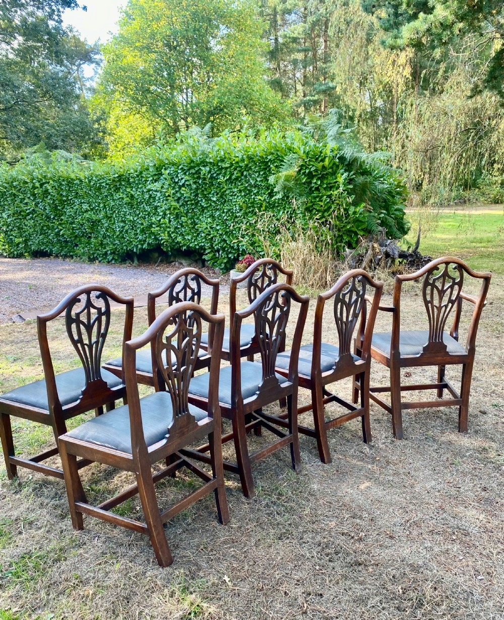 A set of mahogany dining chairs featuring carved openwork back splats, shaped armrests on the carver chairs, and dark fabric upholstered seat pads. View X