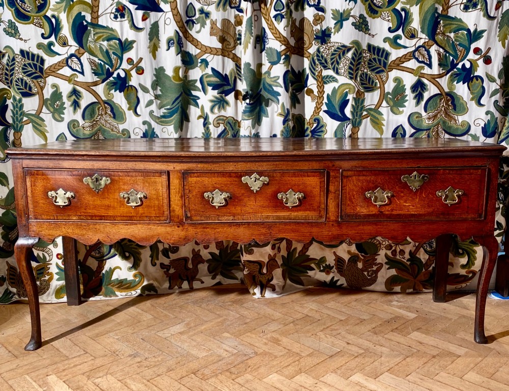 A Georgian oak dresser base featuring three drawers with brass handles, a scalloped apron, and front cabriole legs. View II