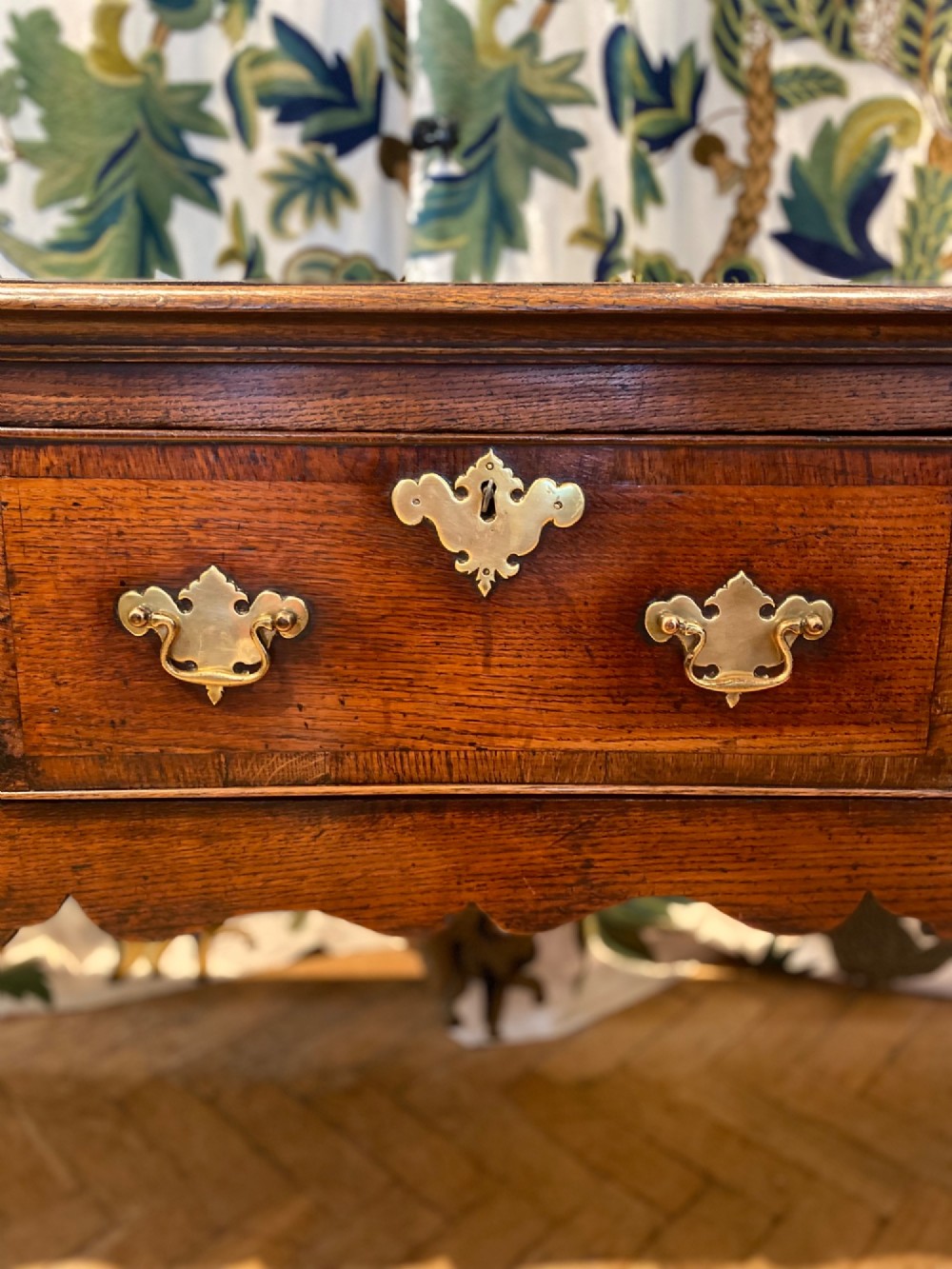 A Georgian oak dresser base featuring three drawers with brass handles, a scalloped apron, and front cabriole legs. View IV