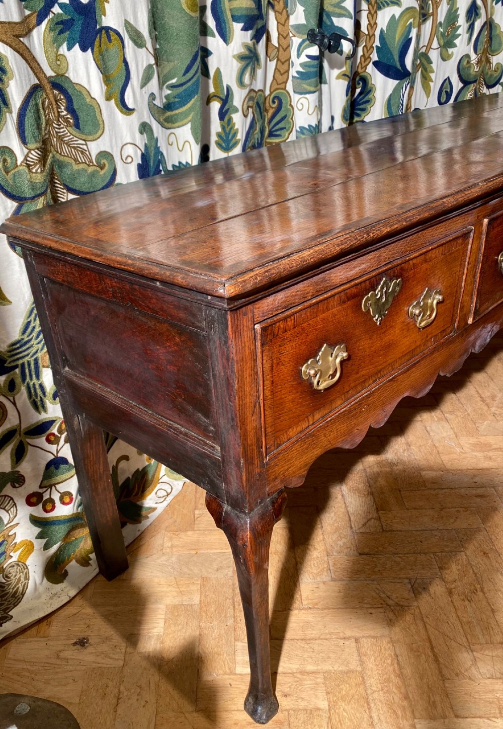A Georgian oak dresser base featuring three drawers with brass handles, a scalloped apron, and front cabriole legs. View V