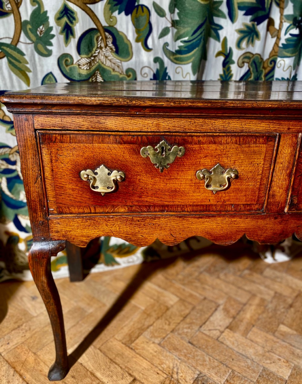 A Georgian oak dresser base featuring three drawers with brass handles, a scalloped apron, and front cabriole legs. View VI