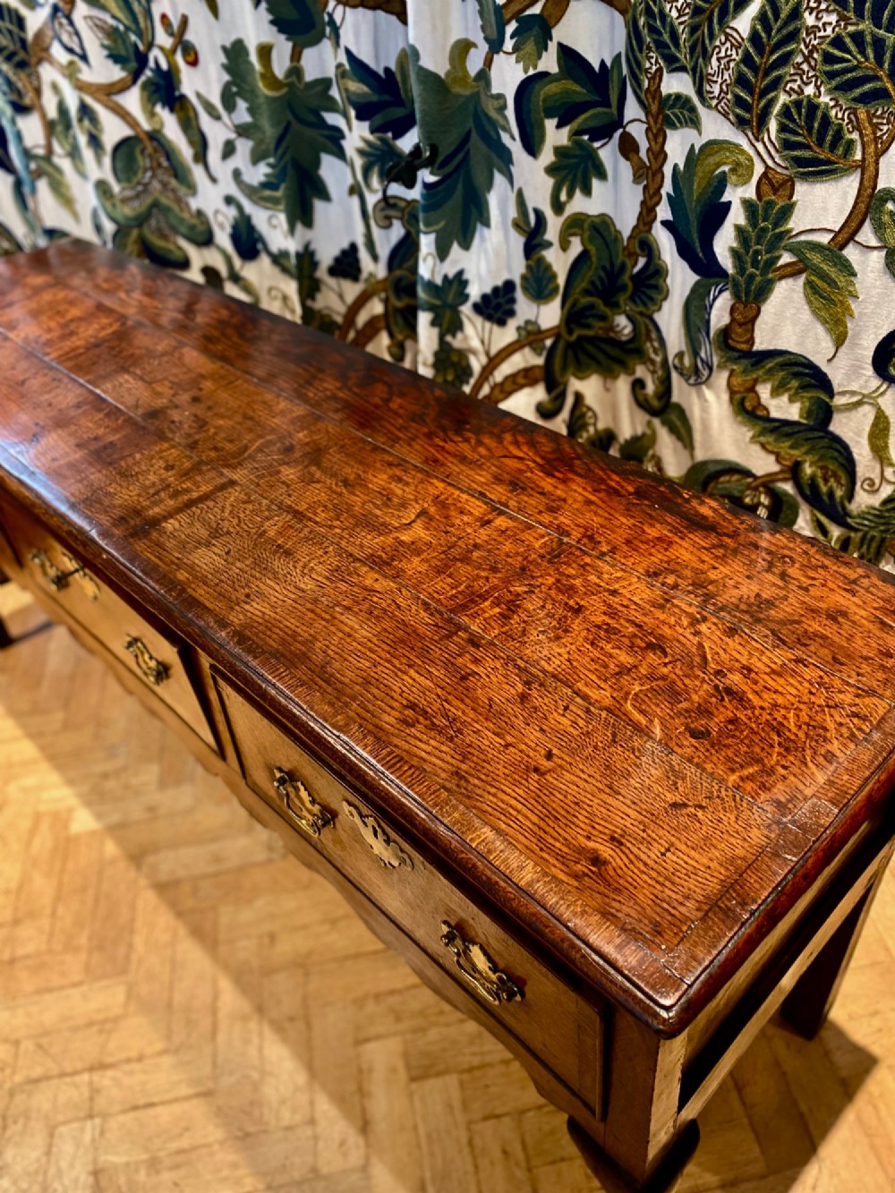 A Georgian oak dresser base featuring three drawers with brass handles, a scalloped apron, and front cabriole legs. View VIII