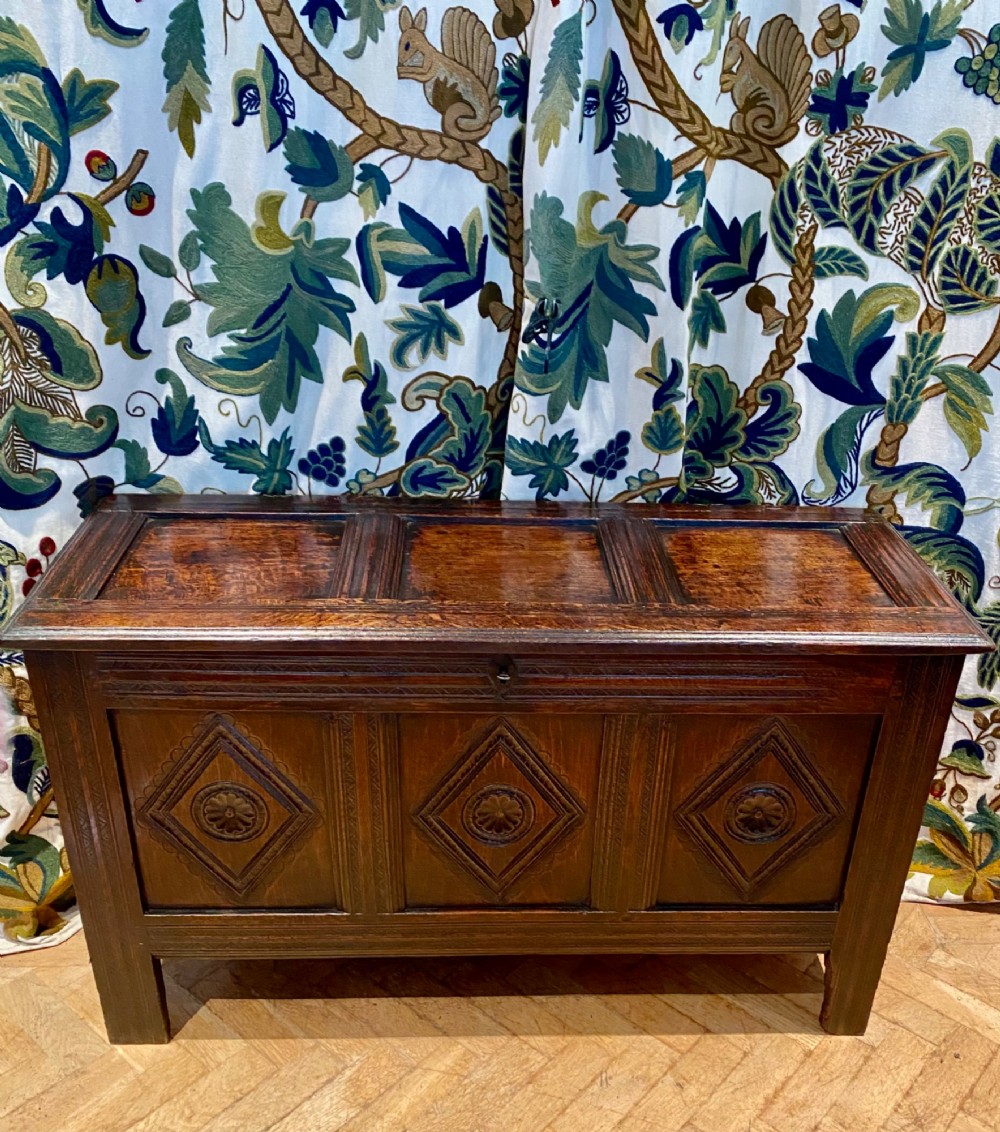 A dark carved oak coffer featuring a three-panel hinged top and three front panels decorated with carved diamond motifs and central rosettes.