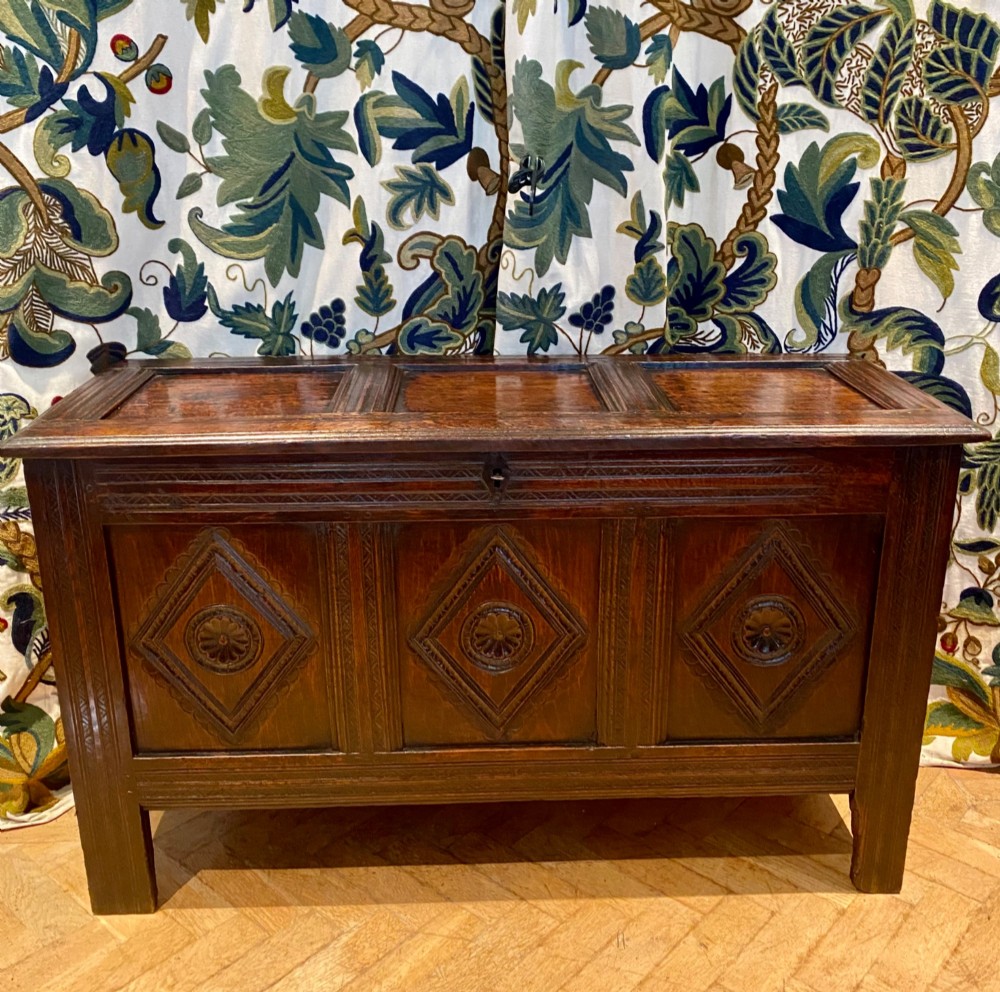 A dark carved oak coffer featuring a three-panel hinged top and three front panels decorated with carved diamond motifs and central rosettes. View II