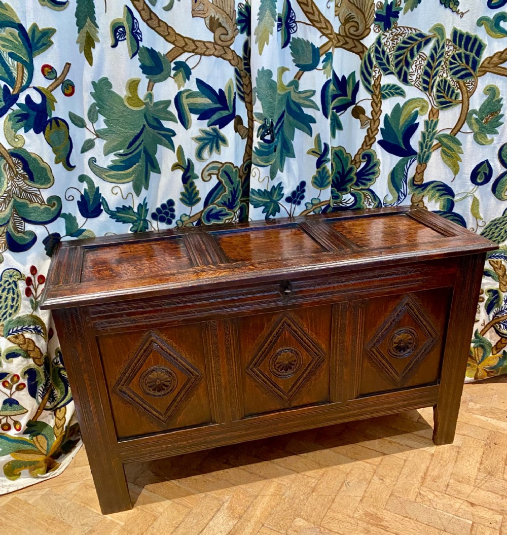 A dark carved oak coffer featuring a three-panel hinged top and three front panels decorated with carved diamond motifs and central rosettes. View III
