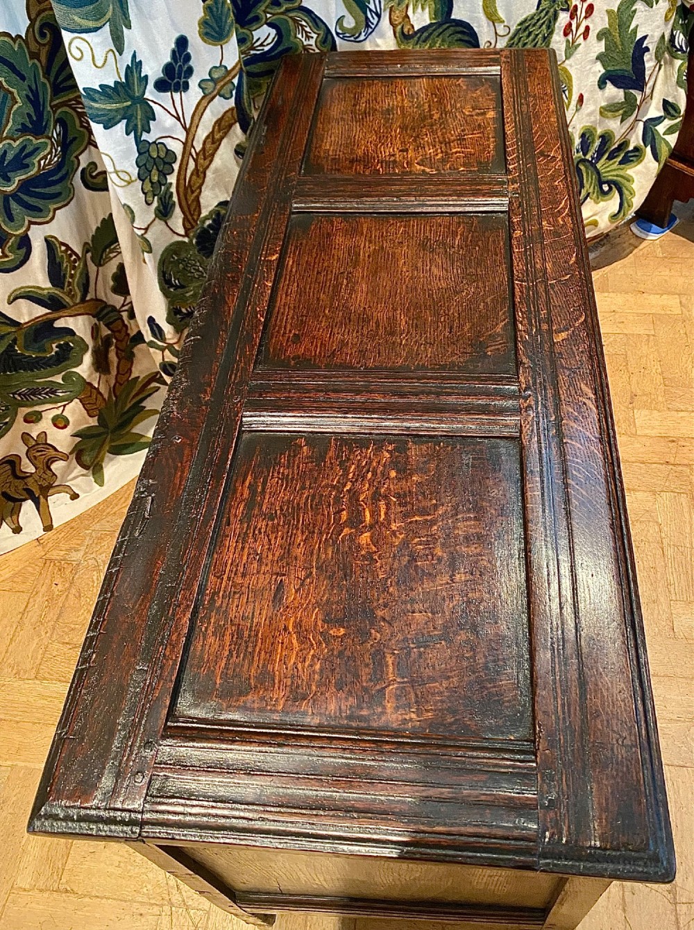 A dark carved oak coffer featuring a three-panel hinged top and three front panels decorated with carved diamond motifs and central rosettes. View V