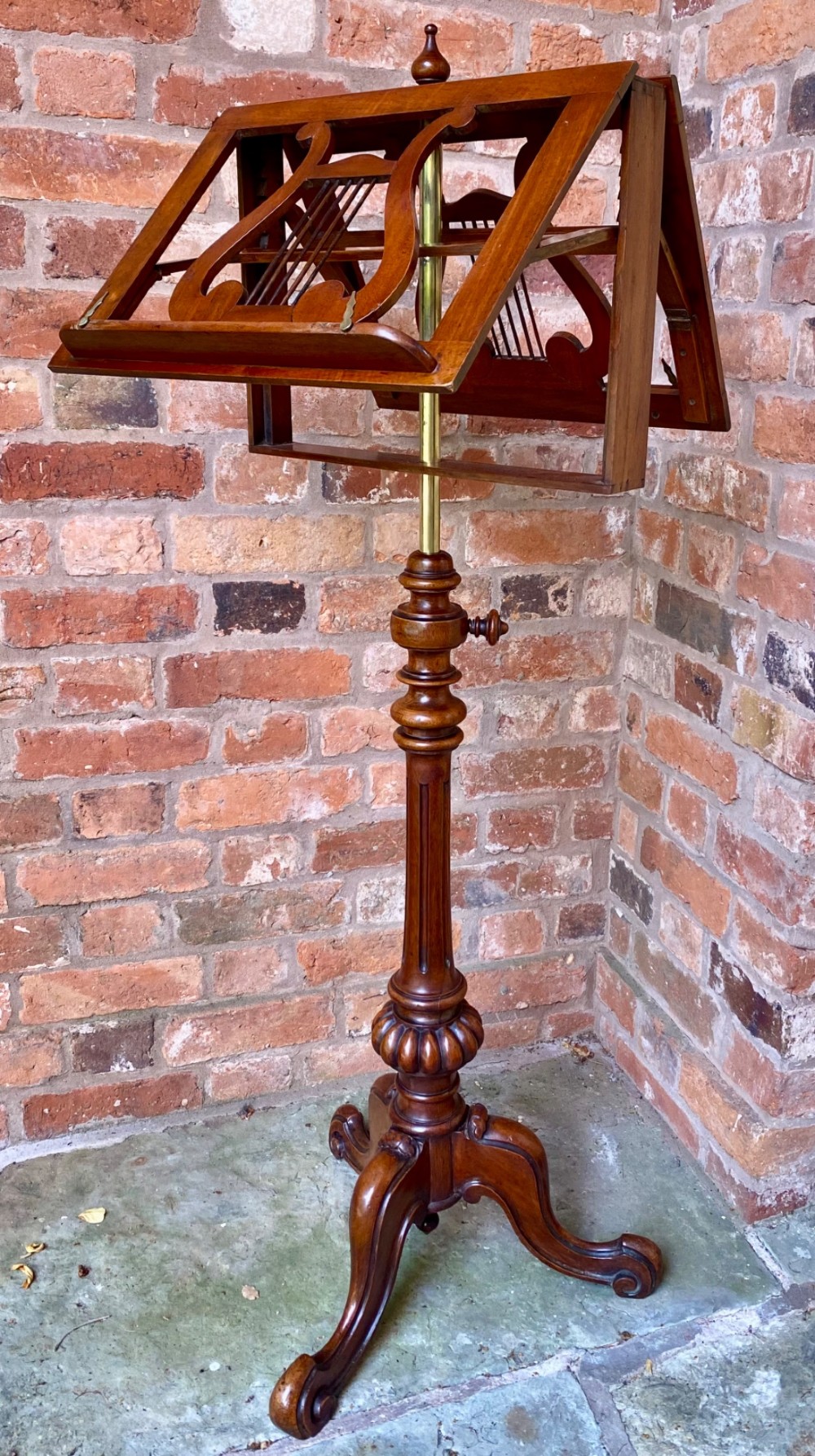 An antique mahogany duet music stand featuring double lyre-shaped rests, an adjustable brass stem, and a turned pedestal base on tripod feet. View II