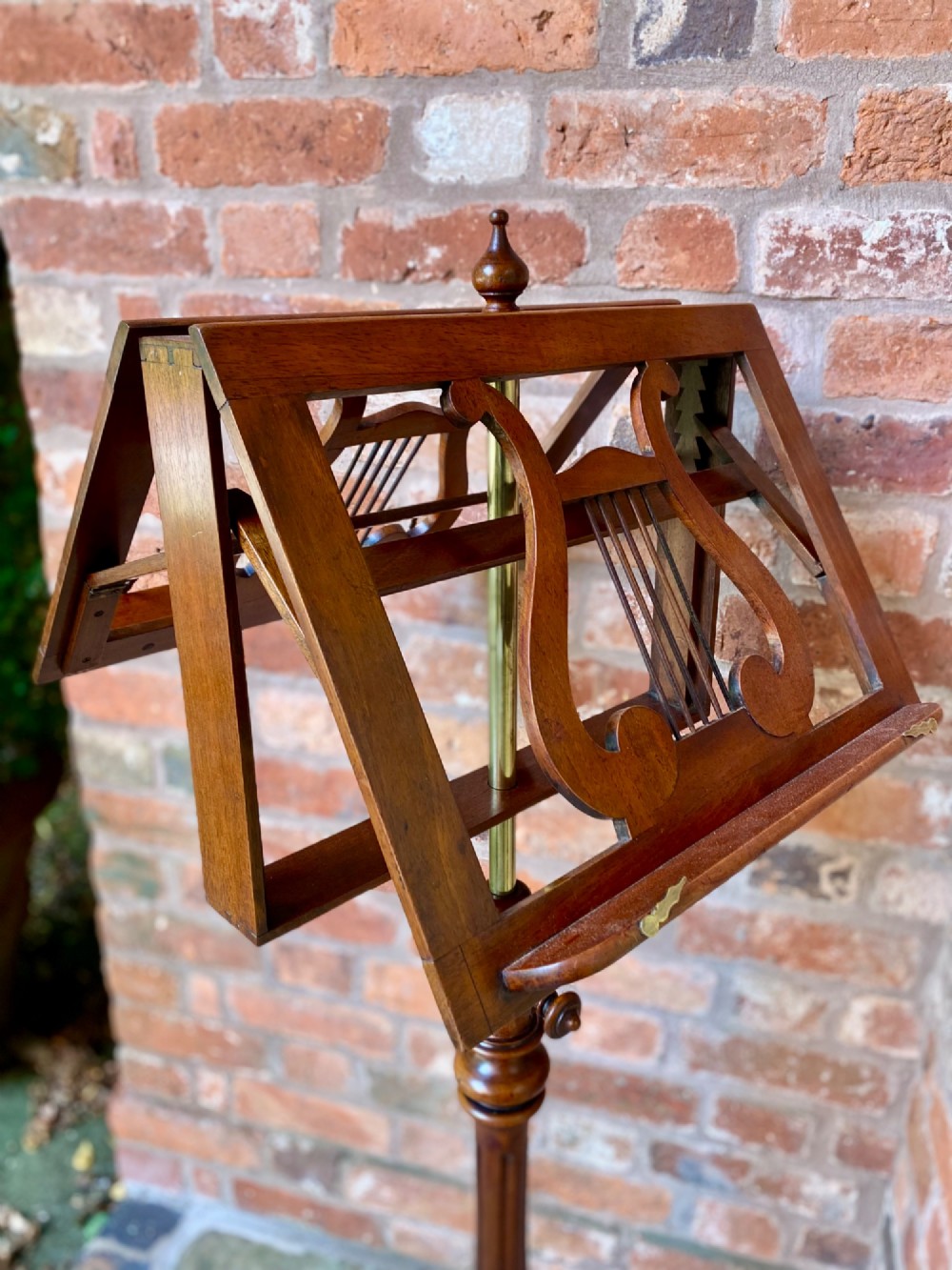 An antique mahogany duet music stand featuring double lyre-shaped rests, an adjustable brass stem, and a turned pedestal base on tripod feet. View IV