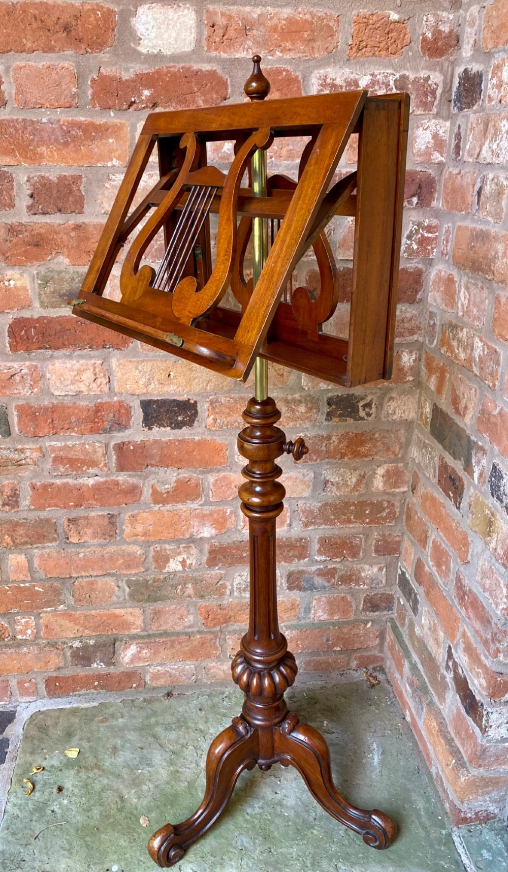 An antique mahogany duet music stand featuring double lyre-shaped rests, an adjustable brass stem, and a turned pedestal base on tripod feet. View V