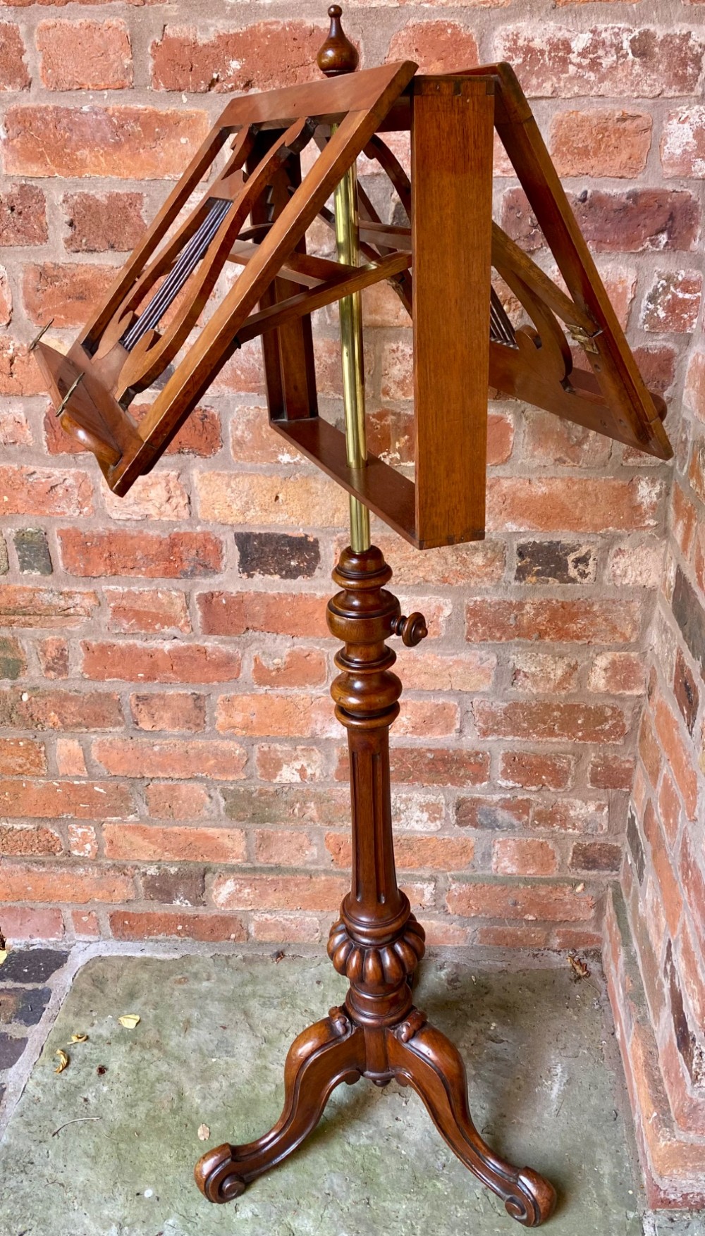 An antique mahogany duet music stand featuring double lyre-shaped rests, an adjustable brass stem, and a turned pedestal base on tripod feet. View VII