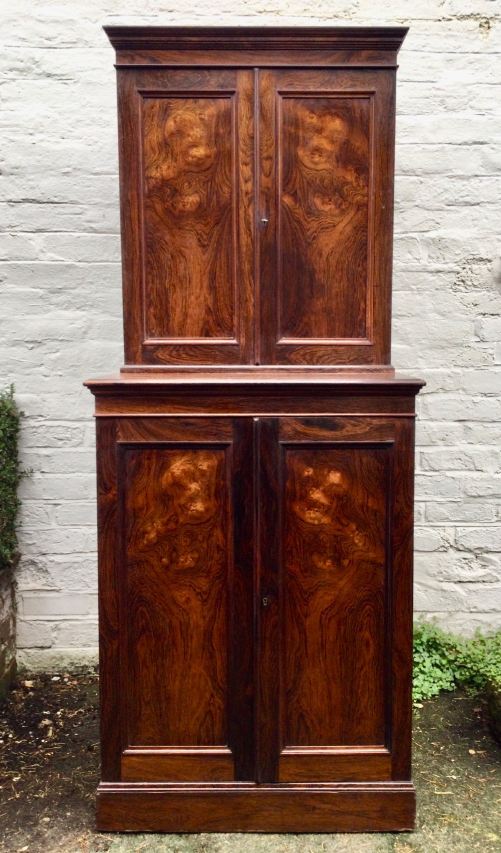 A tall two-tier dark rosewood cabinet with fielded panel doors, a moulded top cornice, and visible wood graining. View II