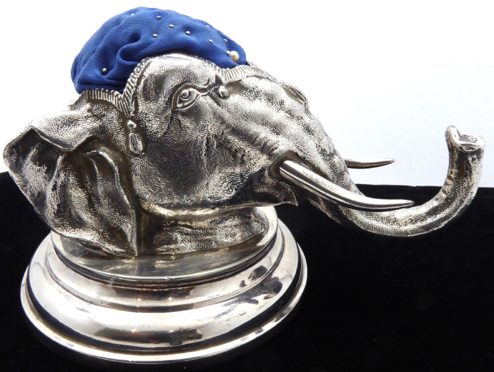 An antique silver pin cushion shaped as an elephant head on a stepped base with a blue velvet fabric insert on top. View VII