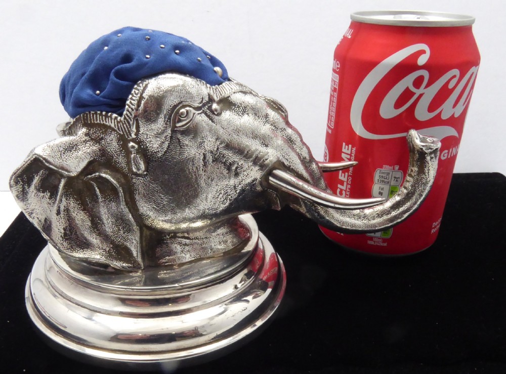 An antique silver pin cushion shaped as an elephant head on a stepped base with a blue velvet fabric insert on top. View XI
