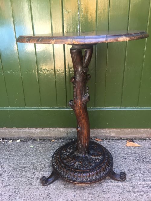 fig 1. A late nineteenth-century dark brown linden wood side table featuring a circular top supported by a carved tree-trunk stem and a foliage-adorned tripod base.
