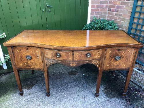 fig 1. A late 18th-century George III mahogany sideboard featuring a serpentine front, floral marquetry inlay, tapering square legs with spade feet, and brass oval handles.