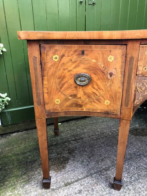 fig 2. A late 18th-century George III mahogany sideboard featuring a serpentine front, floral marquetry inlay, tapering square legs with spade feet, and brass oval handles.